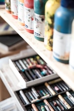 Close-up of colorful tubes of paint neatly arranged on wooden shelves in a cozy shop.