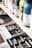 Several paint bottles are neatly arranged on a wooden shelf, with different colors and labels visible. Below the shelf, an open drawer contains various art supplies, including a range of colorful pastels.