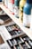 Several paint bottles are neatly arranged on a wooden shelf, with different colors and labels visible. Below the shelf, an open drawer contains various art supplies, including a range of colorful pastels.