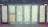 A row of closed doors with frosted glass panels set in a weathered blue frame. The doors are evenly spaced along the front of a building, with two red doors on either end. One of the central panels is covered with a piece of plywood.