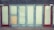 A row of closed doors with frosted glass panels set in a weathered blue frame. The doors are evenly spaced along the front of a building, with two red doors on either end. One of the central panels is covered with a piece of plywood.