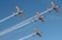 Four aerobatic planes fly in formation against a clear blue sky, leaving trails of smoke behind them. The planes are painted in yellow and blue colors.