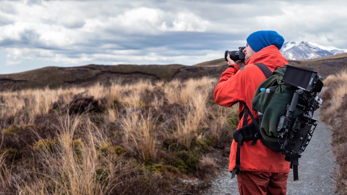 Persona con mochila y cámara fotografiando un paisaje de montaña en Nueva Zelanda, fotografía de muestra