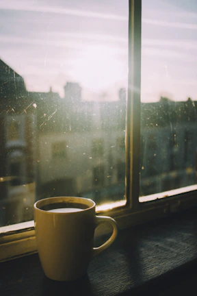 A handmade ceramic mug filled with steaming coffee, placed on a windowsill with morning light.