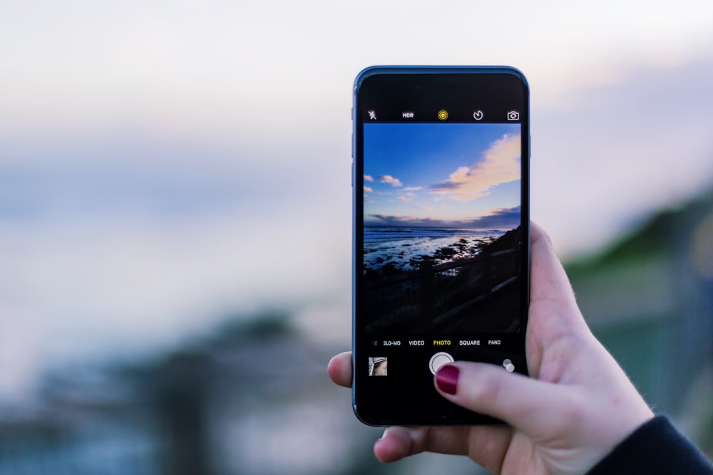 A person taking a picture of the ocean under a mostly clear sky.