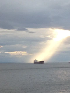 Wide shot of a cargo ship navigating open waters at sunrise