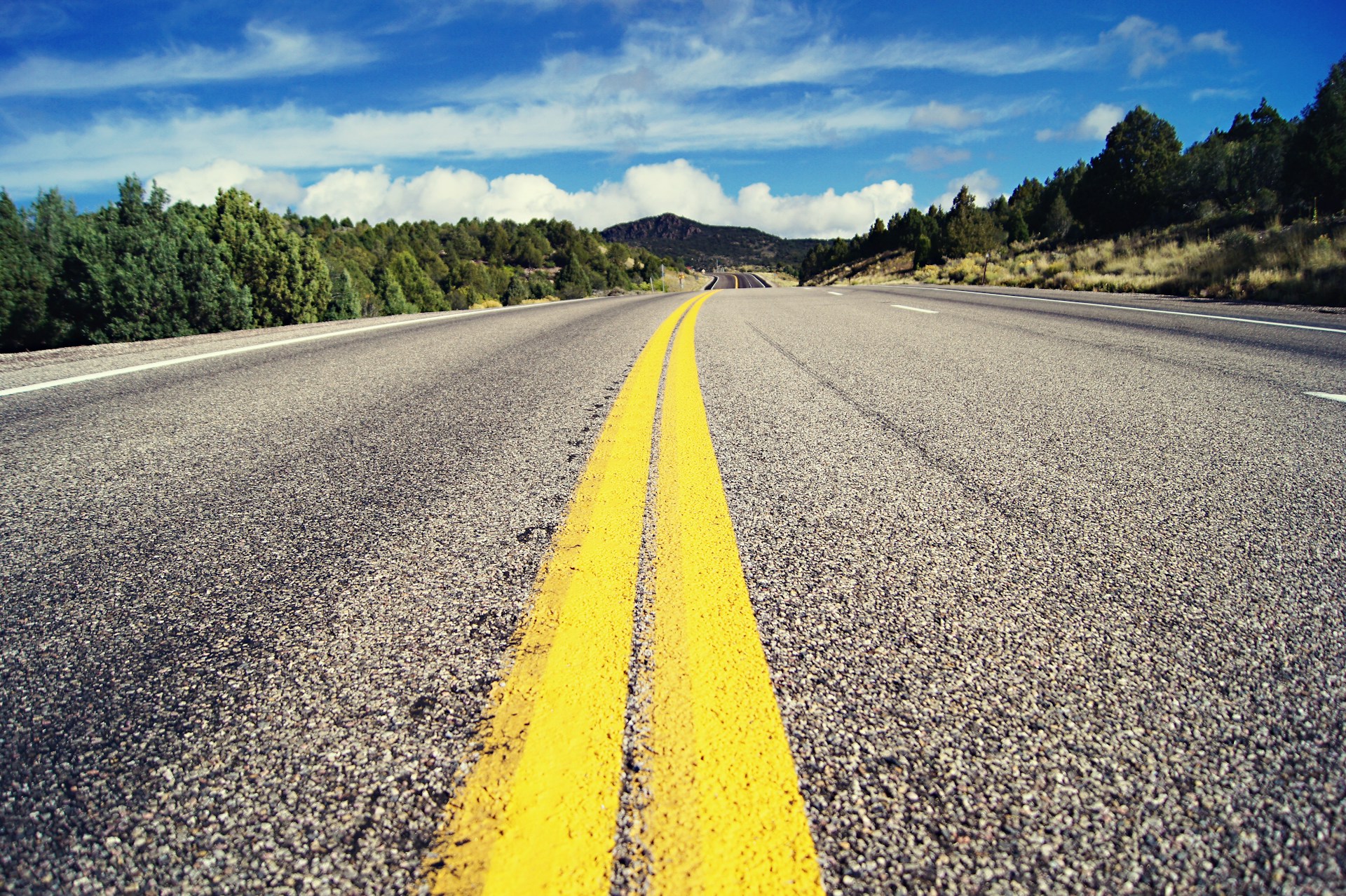 gray concrete road with no vehicle under blue and white skies