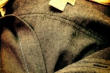 Close-up view of denim fabric showcasing detailed stitching and texture. The fabric appears wrinkled, with visible seam lines and a small fabric tag.