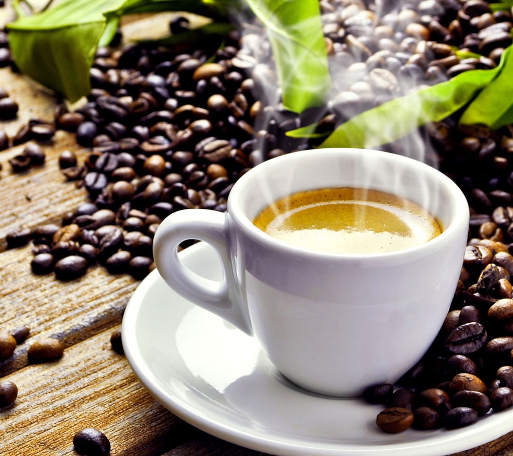 Tasse en céramique blanche sur le dessus d’une soucoupe en céramique blanche entourée de grains de café