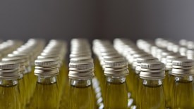 Several rows of identical glass bottles with metal caps are neatly arranged in a pattern. The bottles are filled with a light green liquid and the symmetry of their arrangement creates a sense of order and repetition.