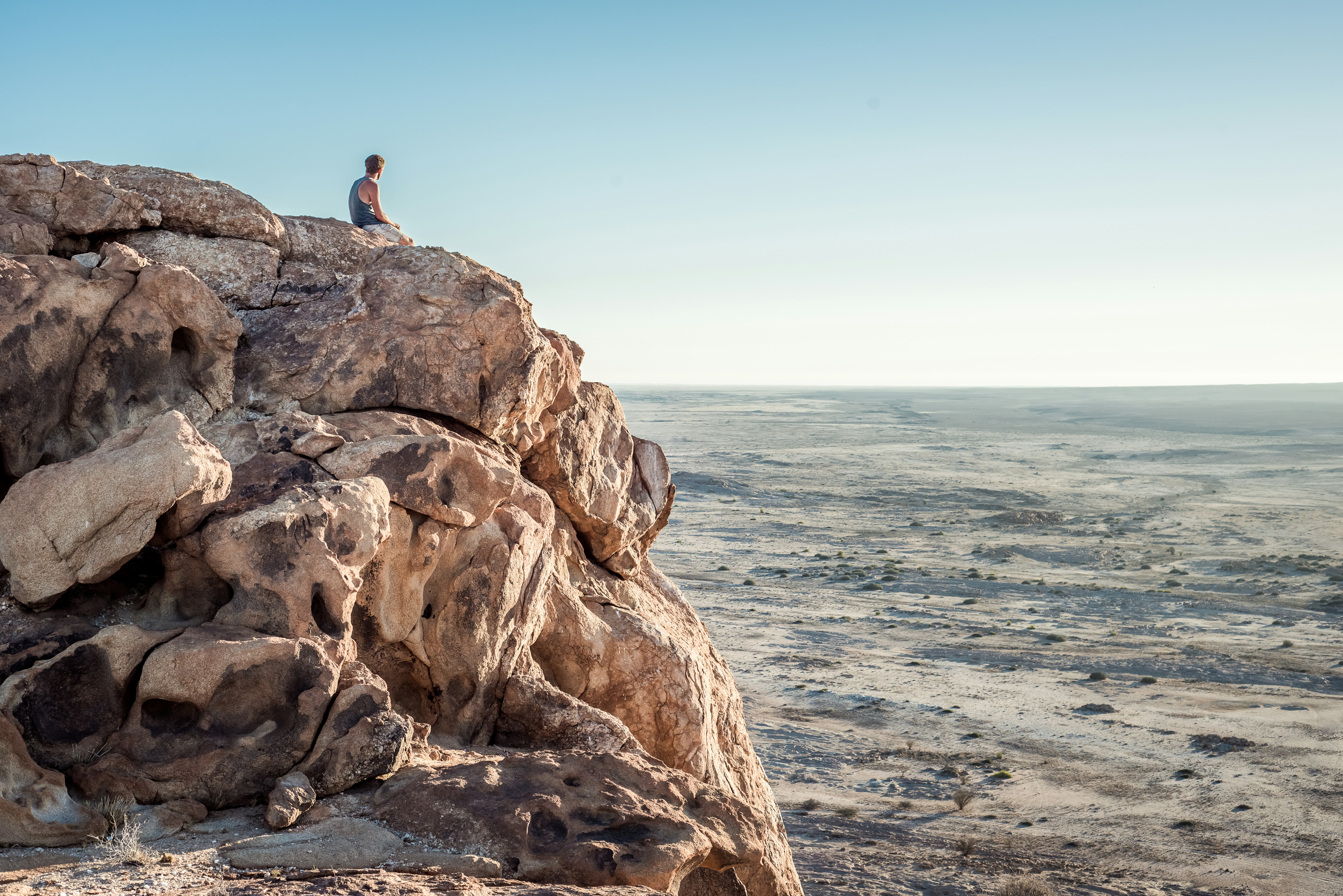 man sitting on top of rock formation near beach