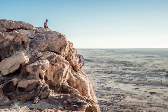 man sitting on top of rock formation near beach
