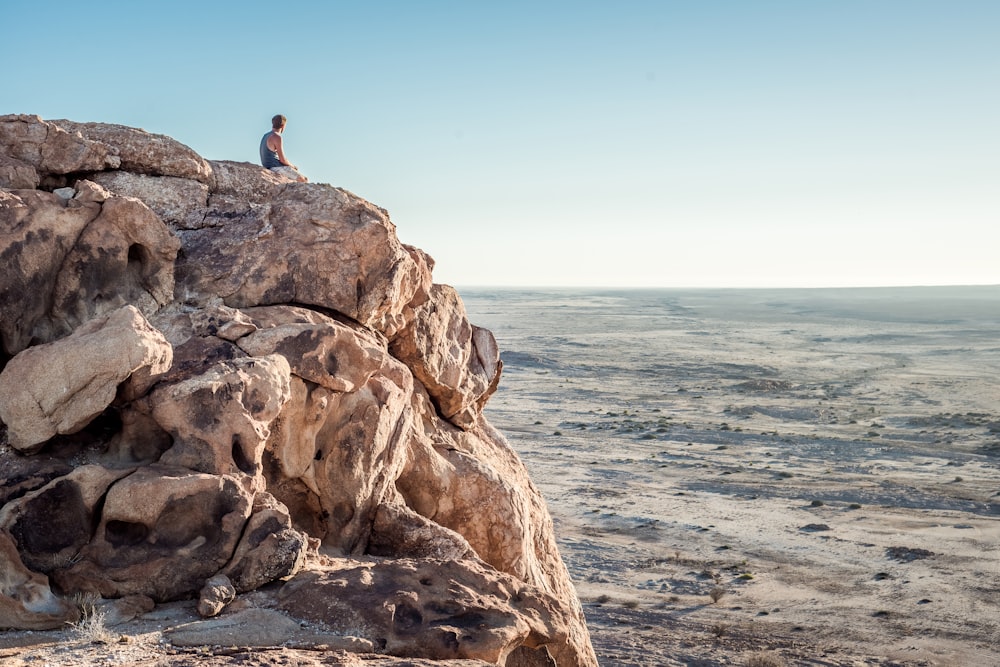 man sitting on top of rock formation near beach