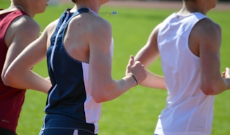 Three individuals wearing sports attire are running together on a track. The focus is on their upper bodies, showcasing their athletic clothing and the movement of their arms as they run.