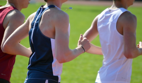 Three individuals wearing sports attire are running together on a track. The focus is on their upper bodies, showcasing their athletic clothing and the movement of their arms as they run.