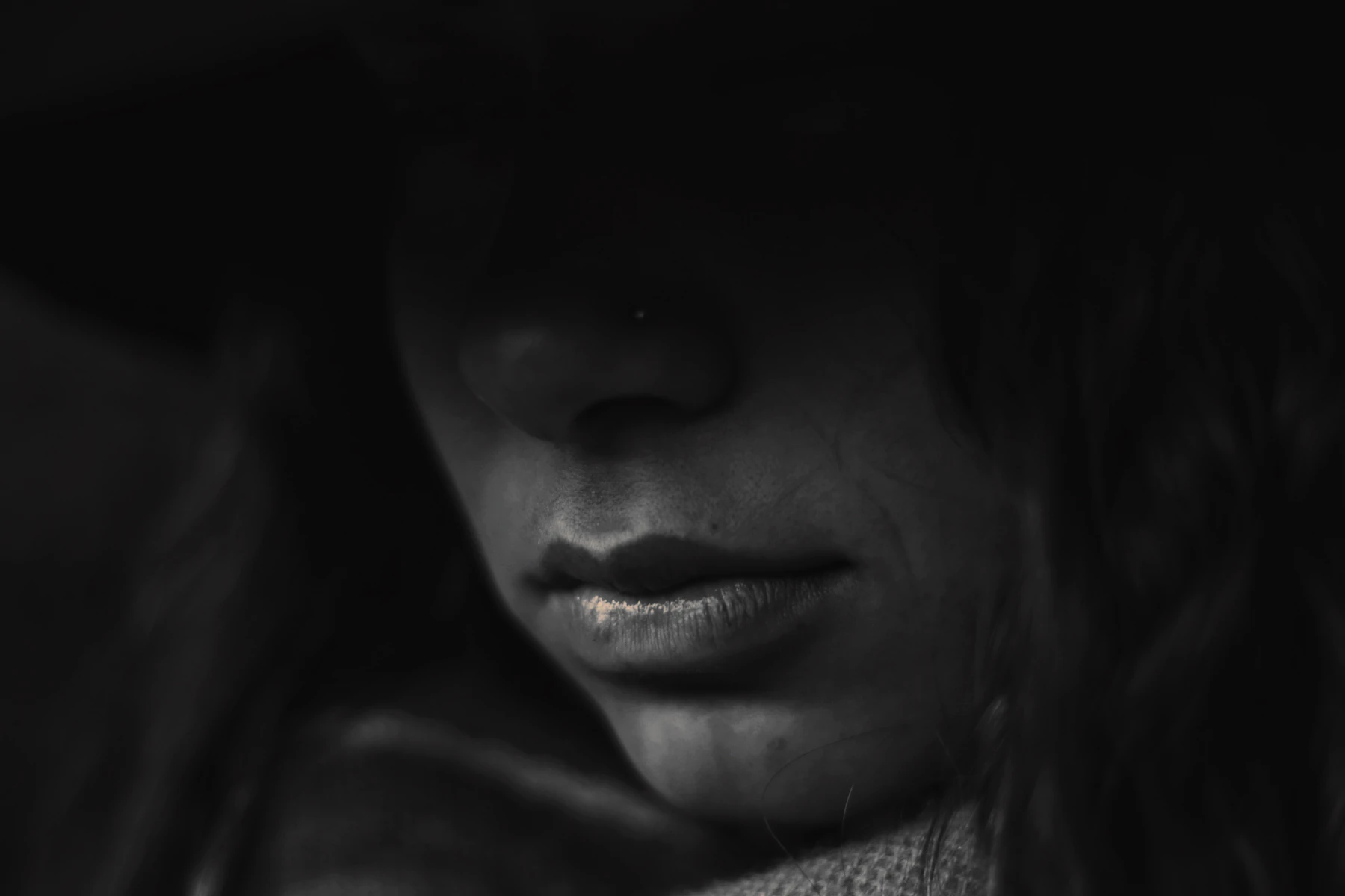Dark black-and-white close-up of the lower half of a person’s face, with closed lips and soft directional lighting.