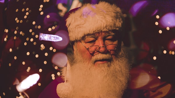 Santa stands among Christmas lights.