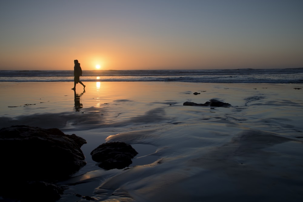 Silhouette einer Person, die am Meeresufer spazieren geht
