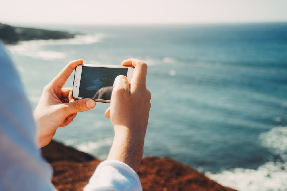 person standing on cliff taking photo of body of water during daytime