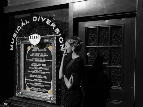 A woman in vintage attire and styled hair stands outside a venue with a decoration sign that reads 'Musical Diversion'. The marquee lists various jazz performances and dates. The scene combines elements of retro fashion with a music theme.