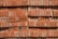 A stack of red perforated bricks arranged neatly in horizontal rows. Each brick has multiple round holes, providing a uniform, textured pattern. The surface shows signs of slight discoloration and wear, possibly from exposure to weather.