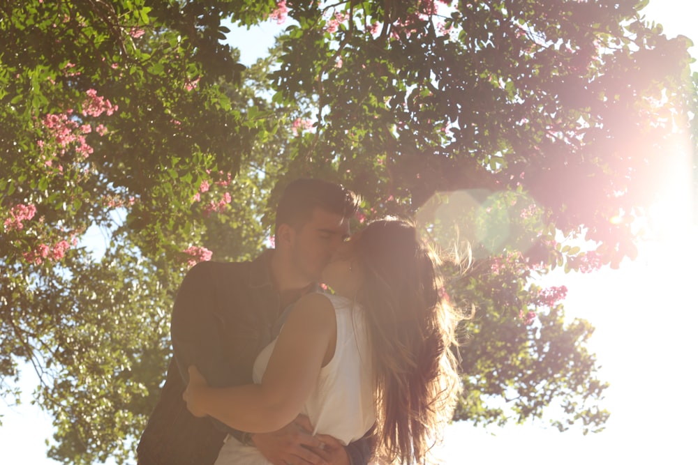 hombre besando a una mujer bajo un árbol verde durante el día