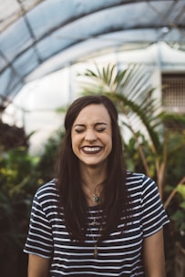 A smiling woman applying nourishing hair care in a sunlit bathroom filled with plants.