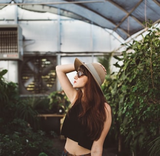 shallow focus photography of woman posing while holding her hat at the garden