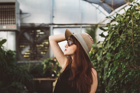 shallow focus photography of woman posing while holding her hat at the garden