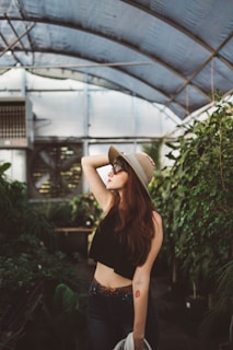 shallow focus photography of woman posing while holding her hat at the garden