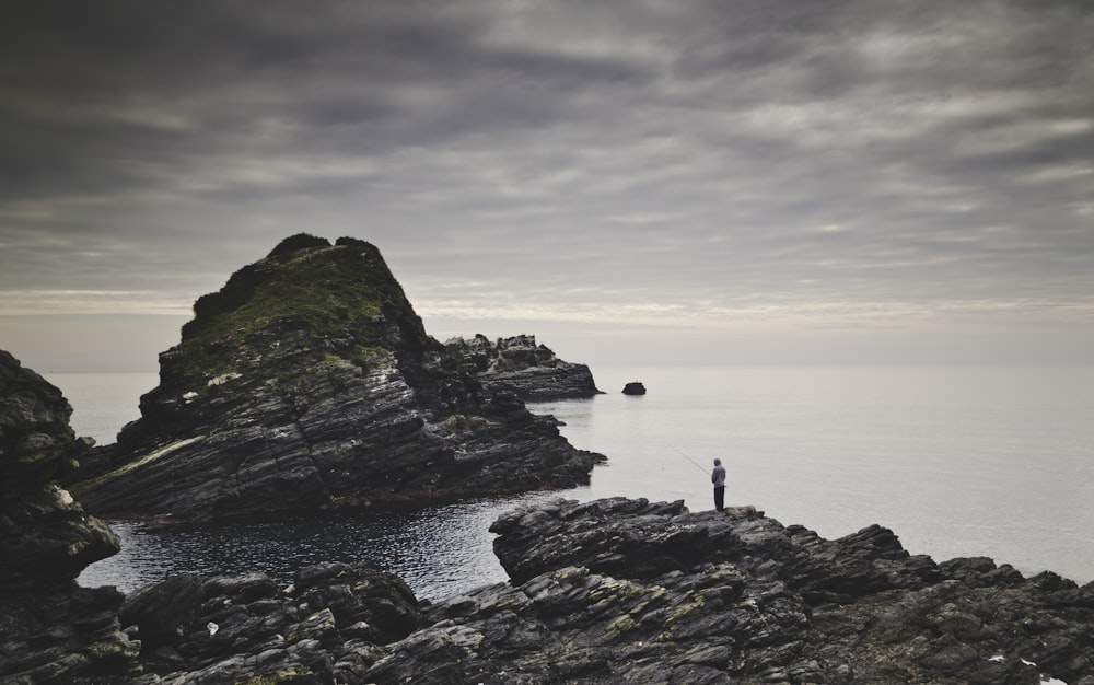 person standing on brown rock formation by the sea during daytime