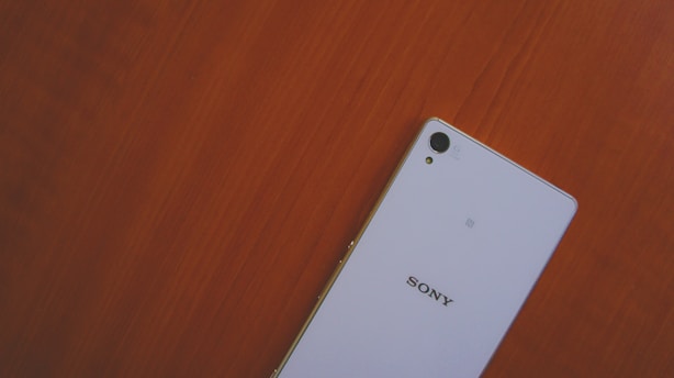 A smartphone with a white back featuring the Sony logo is positioned on a wooden surface.