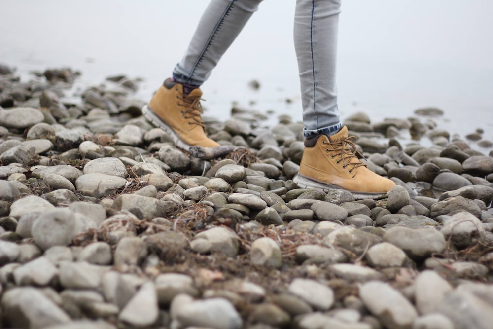 person wearing brown shoes walking through stoned seashore