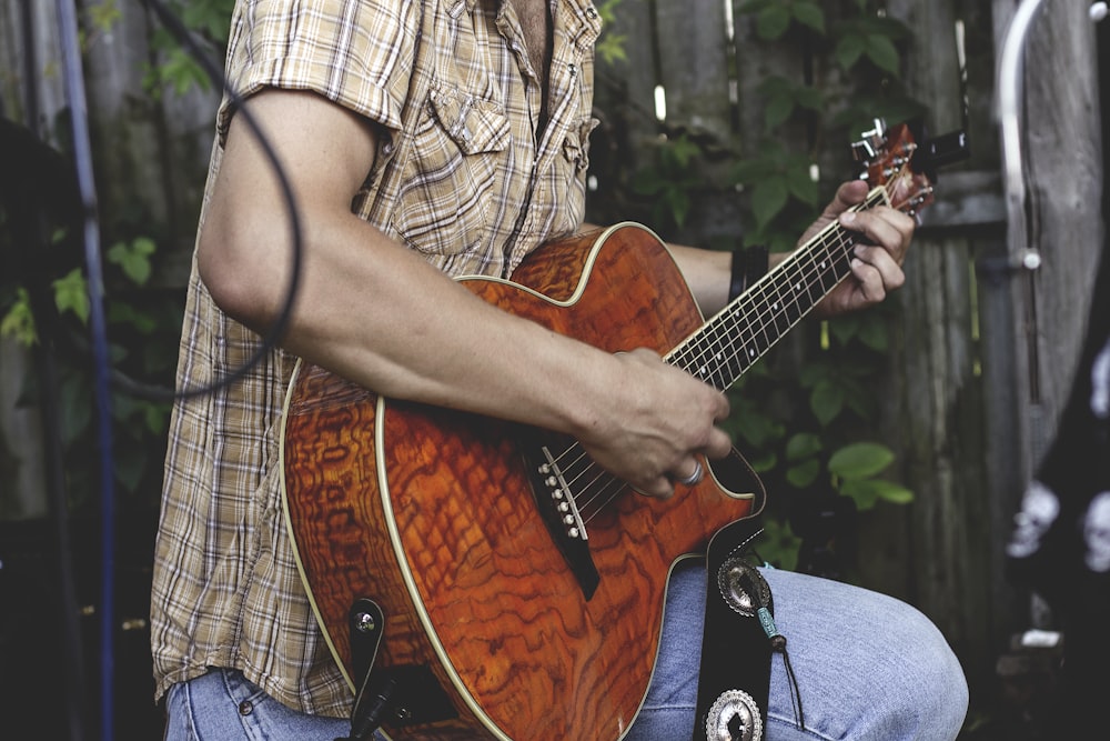 Persona sosteniendo una guitarra marrón al aire libre