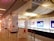 An indoor exhibition area with several display boards and glass cases, featuring information panels with text and images. The ceiling has white draped fabric, and the area is lit with overhead lights. Red ropes and stanchions are used for crowd control.