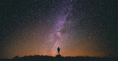 silhouette of man standing on rock while looking in sky