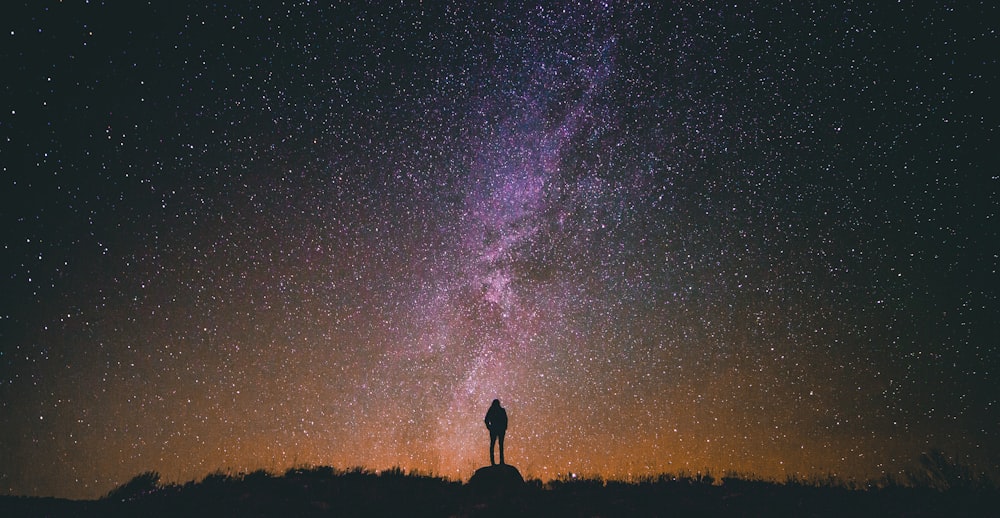 Silhouette eines Mannes, der auf einem Felsen steht, während er in den Himmel schaut