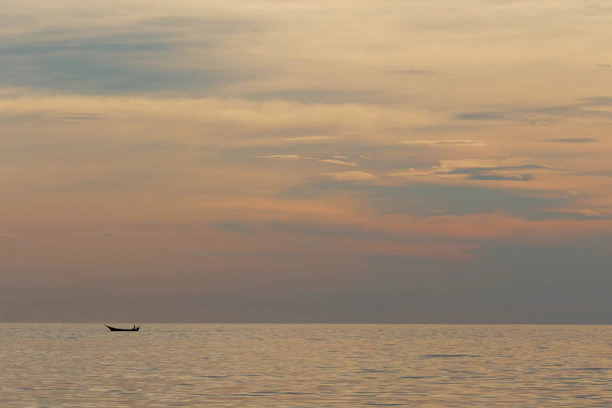Wide-angle view of a boat cutting through calm, sunlit waters under a vast open sky at dusk.