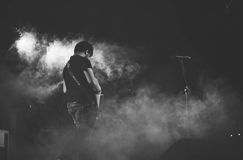 grayscale photography of man performing guitar on stage