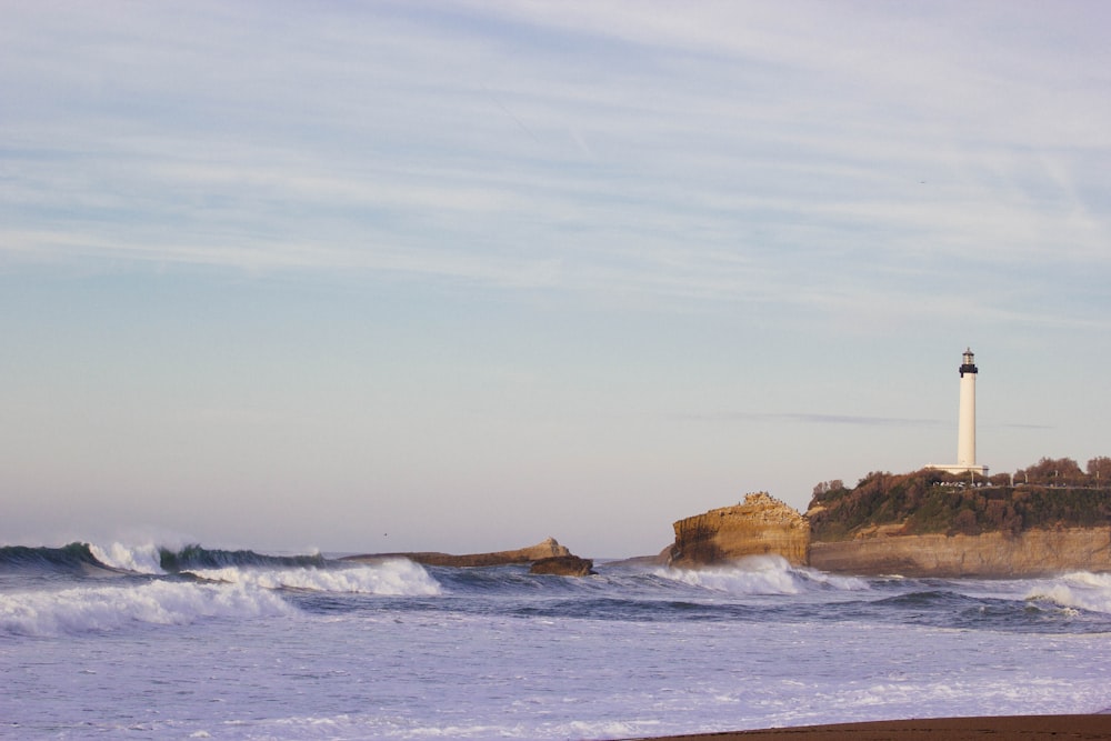 farol na colina perto do oceano sob o céu azul durante o dia