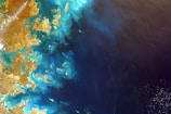 A satellite image showing a coastal area with intricate patterns of land and water. The land appears arid and brown, while the water is a rich mix of blues and turquoise.