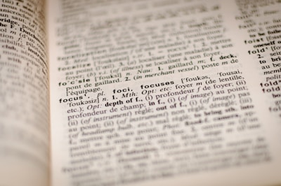 A close-up view of a dictionary page with the word 'focus' highlighted and underlined in black along with its definition and related terms. The text is in English and includes phonetic transcriptions and usage in different contexts. Surrounding words and definitions are also partially visible.