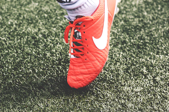 Close-up of a footballer lacing up new boots on a wet grass pitch.