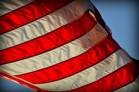 A close-up of a waving flag featuring alternating red and white stripes, suggesting motion and vibrancy against a clear blue sky.