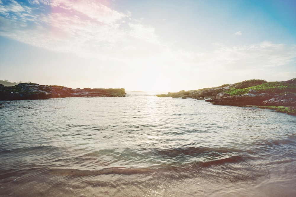 calm water with brown and green rock formation at daytime