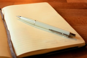 An elegant, clean notebook open on a white desk with a charcoal black pen placed diagonally.