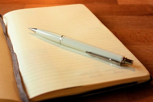 An open journal with a pen resting on a wooden table.