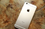 A gold-colored smartphone lies face down on a wooden surface showing its back panel with a prominent logo and camera lens at the top.