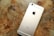 A gold-colored smartphone lies face down on a wooden surface showing its back panel with a prominent logo and camera lens at the top.