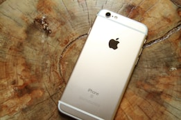 A gold-colored smartphone lies face down on a wooden surface showing its back panel with a prominent logo and camera lens at the top.